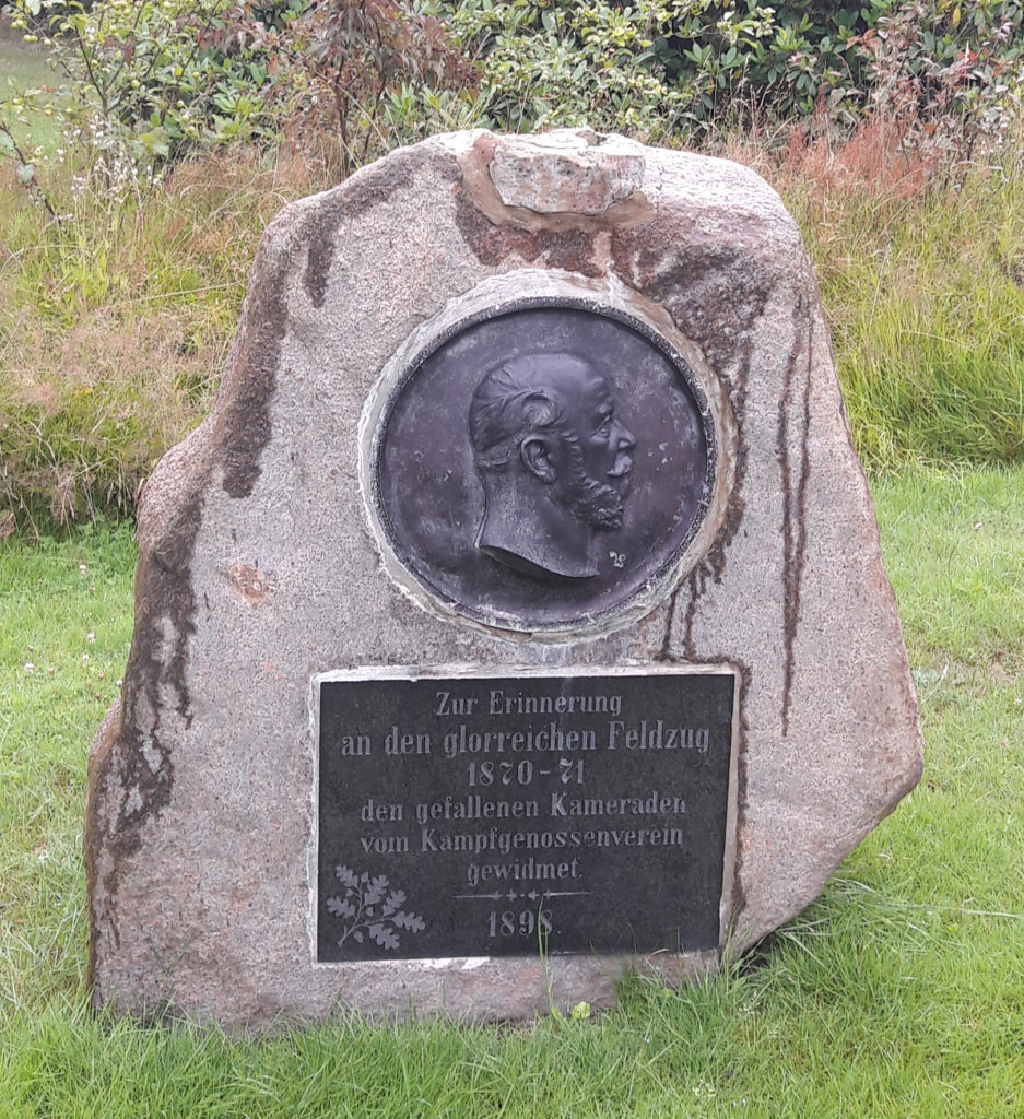 Das Kriegerdenkmal in 2019, ein Stein mit Inschrift und einem seitlichen Portraitbild.