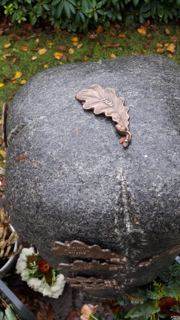 Ein Grabstein mit gemeinamer Ablagemöglichkeit, darauf mehrere kleine Metallblätter.