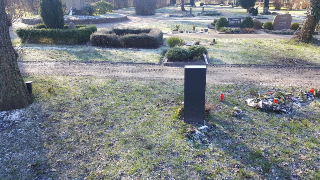 Ein einzelner Grabstein in Rasen.