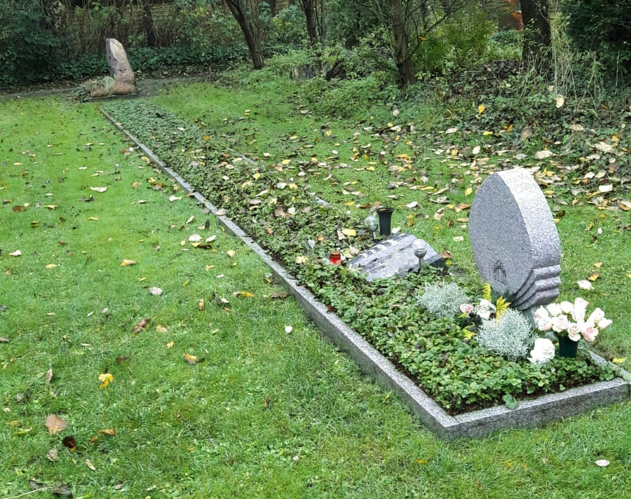Eine grün bepflanzte Grabreihe mit drei Grabsteinen.