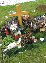 Eine Kindergrabstätte mit einem Holzkreuz und viel Grabschmuck.
