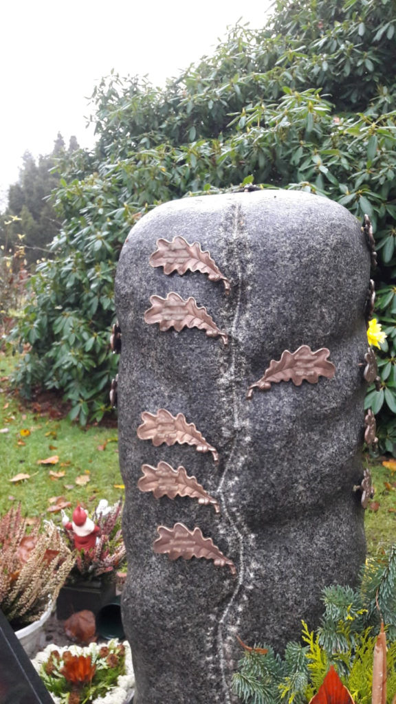 Ein Grabstein mit gemeinamer Ablagemöglichkeit, darauf mehrere kleine Metallblätter.