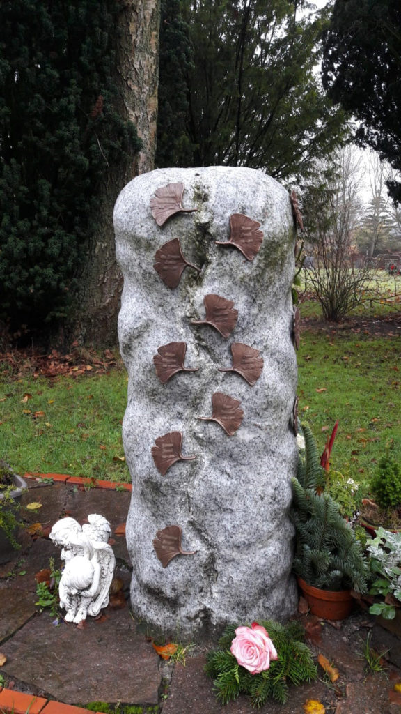 Ein Grabstein mit gemeinamer Ablagemöglichkeit, darauf mehrere kleine Metallblätter.