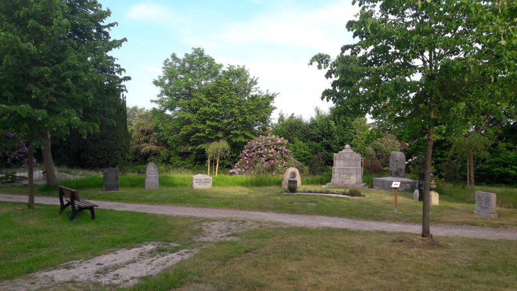 8 historische Grabsteine auf dem Friedhof Niebüll, davor eine Bank.