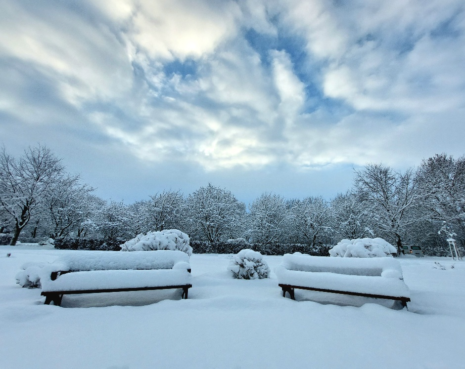 Zwei Bänke stehen auf dem Friedhof. Der Boden und die Bänke sind mit 30cm Neuschnee bedeckt.