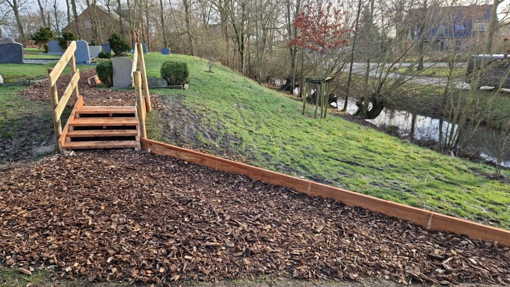 Eine Holztreppe mit beidseitigen Handläufen führt einen Hügel zum Friedhof hinauf.