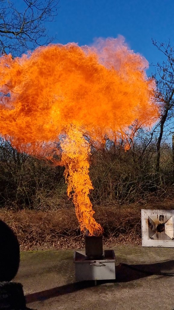 Eine große hohe Flamme steigt aus einem Metallkasten hervor.