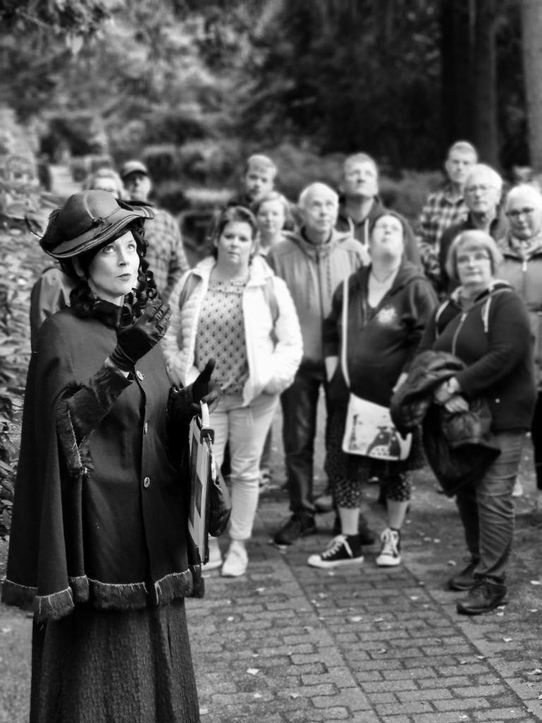 Eine schwarz gekleidete Frau im Vordergrund und einige Zuhöher im Hintergrund.